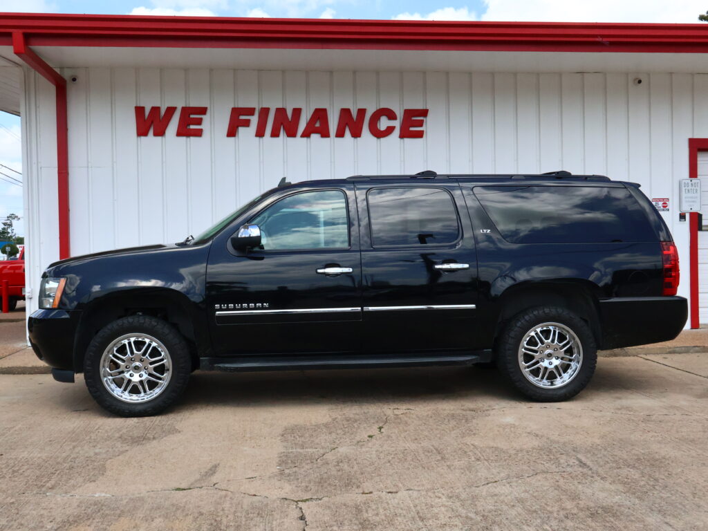 Black Chevrolet Suburban LTZ SUV parked in front of a white building with a red WE FINANCE sign above it
