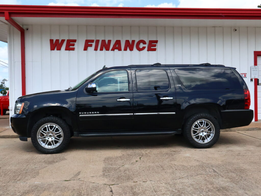 Black Chevrolet Suburban LTZ SUV parked in front of a white building with a red WE FINANCE sign above it