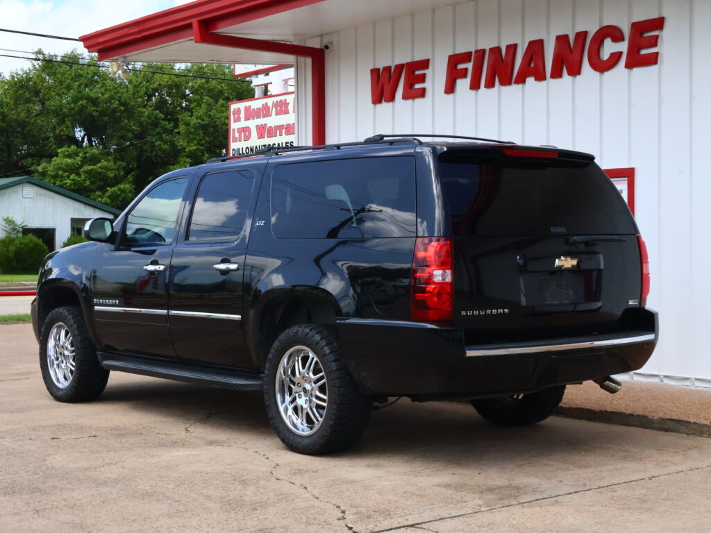 Black Chevrolet Suburban SUV parked in front of a white building with a red 'WE FINANCE' sign above it.