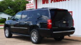 Black Chevrolet Suburban SUV parked in front of a white building with a red 'WE FINANCE' sign above it.