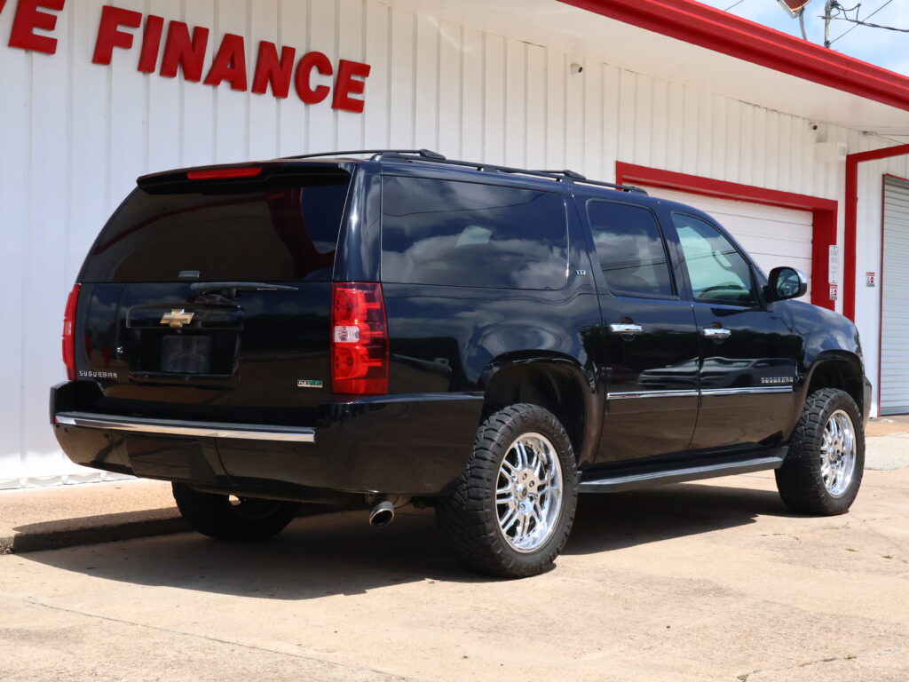 Black Chevrolet Suburban SUV parked in front of a white building with a red 'FINANCE' sign above.