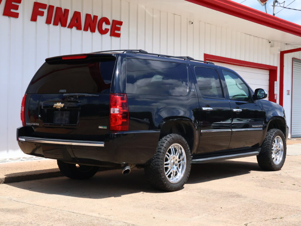 Black Chevrolet Suburban SUV parked in front of a white building with a red 'FINANCE' sign above.