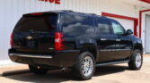 Black Chevrolet Suburban SUV parked in front of a white building with a red 'FINANCE' sign above.
