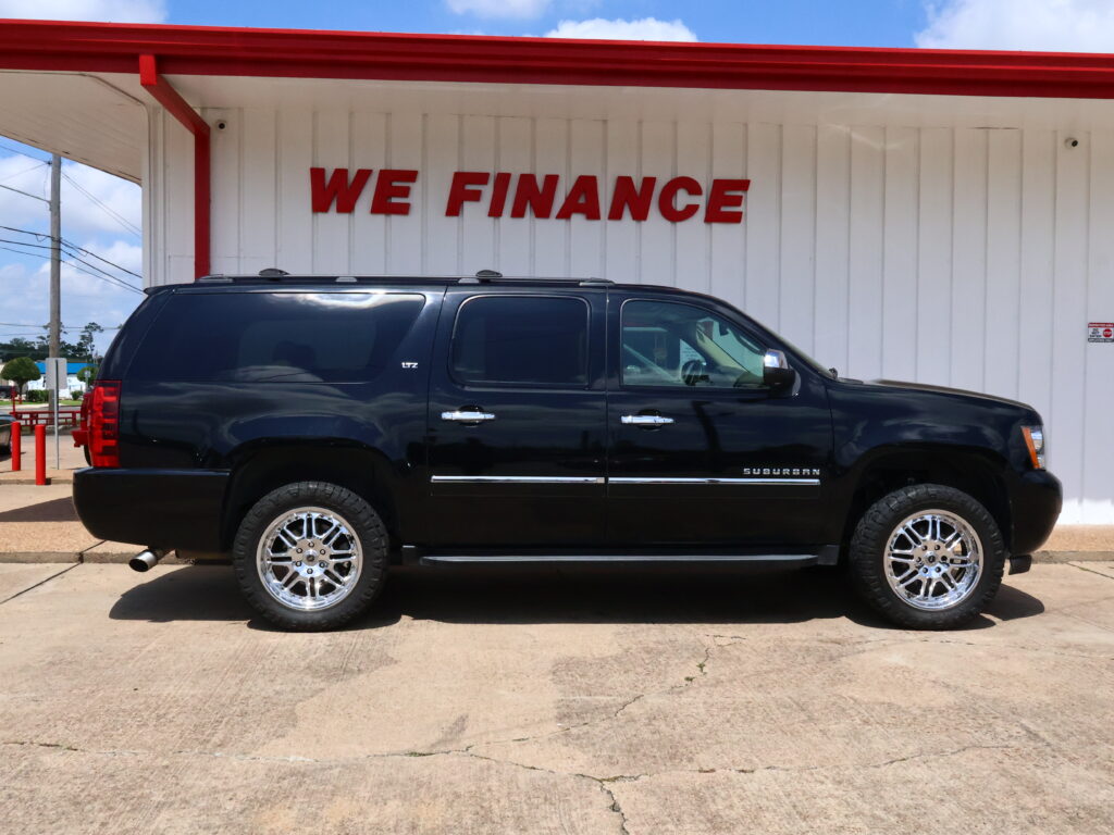 Black SUV (Suburban) parked in front of a white wall with bold red 'WE FINANCE' sign above.