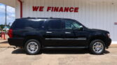 Black SUV (Suburban) parked in front of a white wall with bold red 'WE FINANCE' sign above.