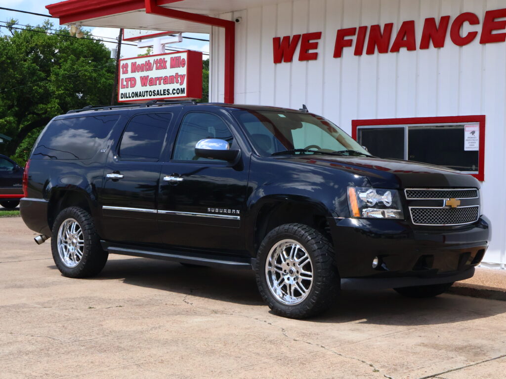 Black Chevrolet Suburban parked in front of a white dealership building with a bold red 'WE FINANCE' sign and red trim.