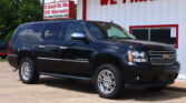 Black Chevrolet Suburban parked in front of a white dealership building with a bold red 'WE FINANCE' sign and red trim.