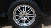 Close-up of a chrome alloy wheel and large all-terrain tire mounted on a dark vehicle, wheel filling the frame.