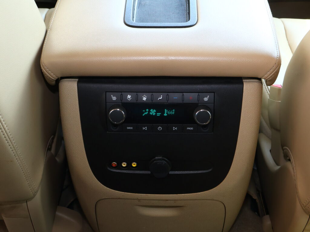 Beige car rear center console with climate control buttons and a small display screen below the armrest.