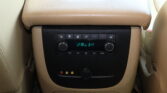 Beige car rear center console with climate control buttons and a small display screen below the armrest.