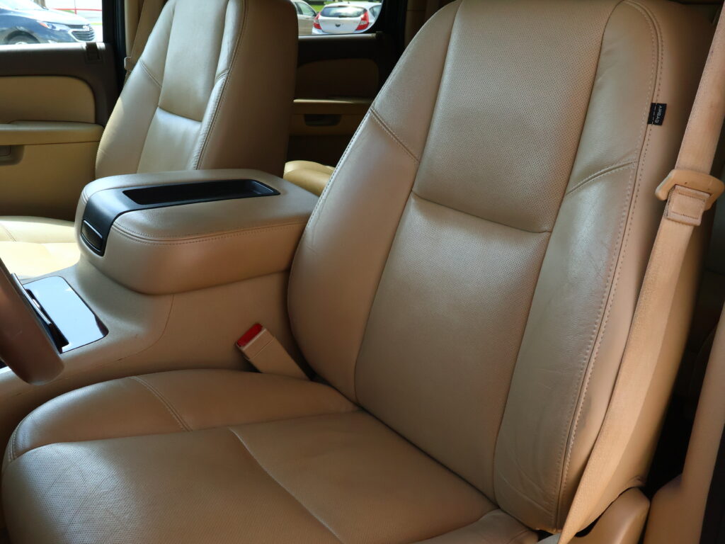 Tan leather car interior showing front seats, center console, and visible beige seatbelt in the passenger area.