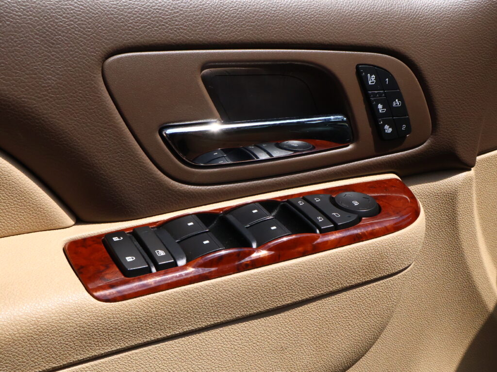 Brown leather car door interior with chrome door handle and window/seat control panel on the armrest, including memory seat buttons.
