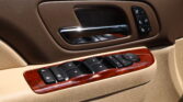 Brown leather car door interior with chrome door handle and window/seat control panel on the armrest, including memory seat buttons.