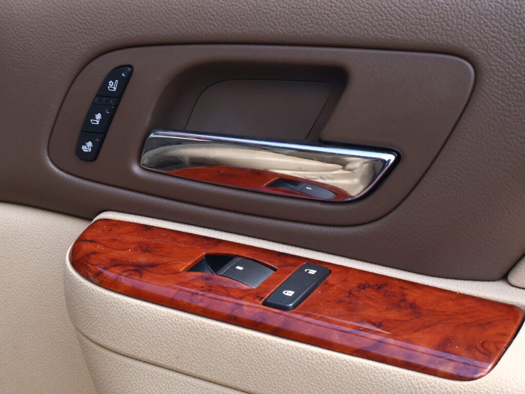 Car door panel with window/lock control buttons and a chrome door handle on wood trim.