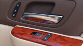 Car door panel with window/lock control buttons and a chrome door handle on wood trim.