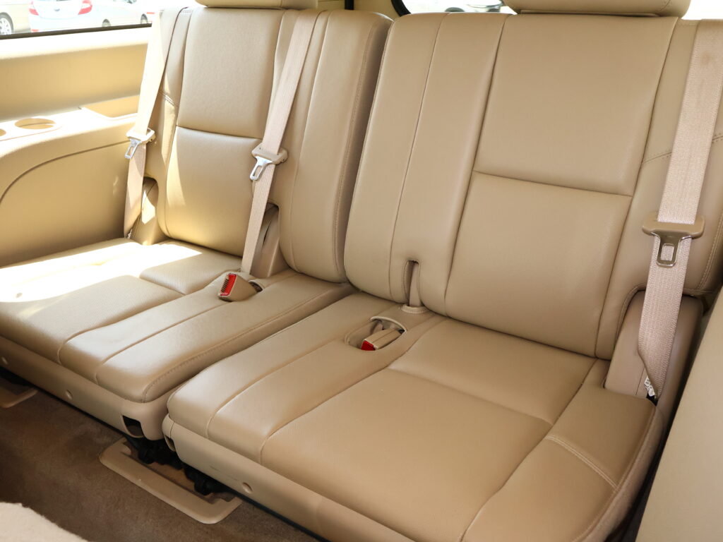 Beige leather back seat row in a car with three seating positions and visible seat belts.