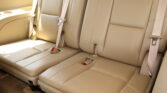 Beige leather back seat row in a car with three seating positions and visible seat belts.
