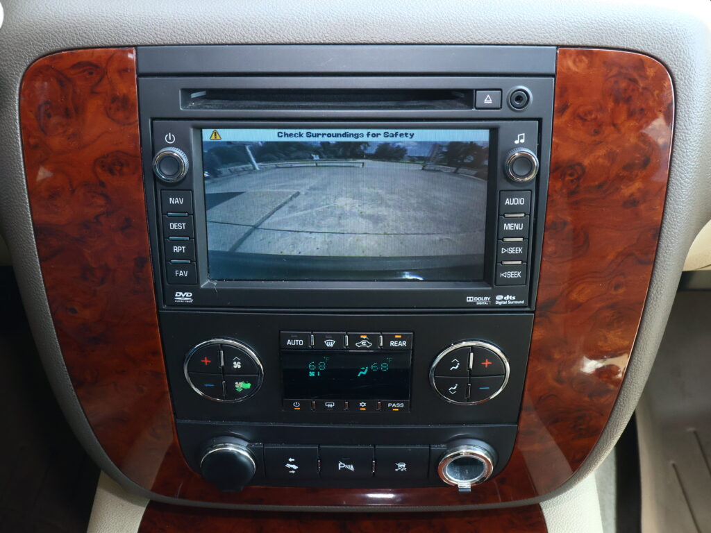 Car infotainment screen showing the rear‑view camera feed in a parking lot scene with 'Check Surroundings for Safety' message