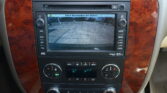 Car infotainment screen showing the rear‑view camera feed in a parking lot scene with 'Check Surroundings for Safety' message