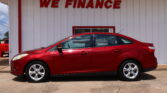 Red sedan parked in front of a white building with a bold red 'WE FINANCE' sign on the wall.