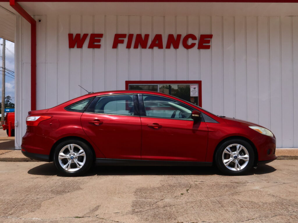 Red car parked in front of a white wall with large red 'WE FINANCE' lettering above it.