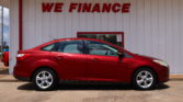 Red car parked in front of a white wall with large red 'WE FINANCE' lettering above it.