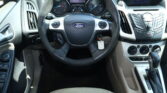 Interior view of a Ford car dashboard with steering wheel, instrument cluster, and center console controls visible from the driver’s seat.