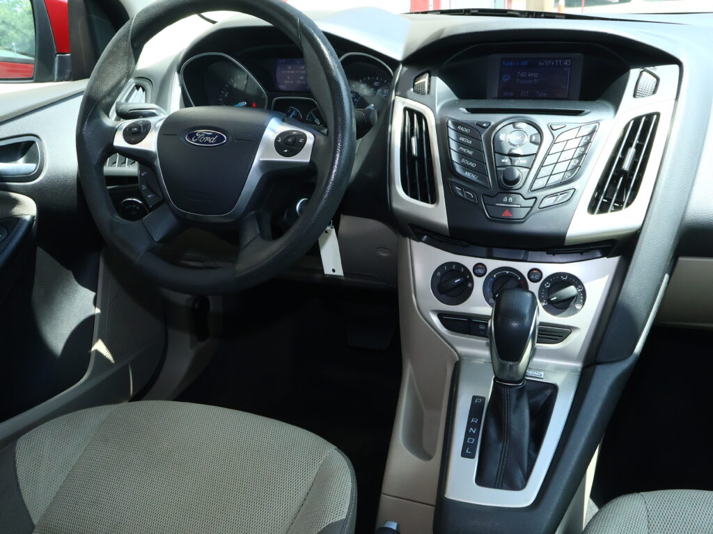 Inside a Ford car: steering wheel with control buttons, center console, and gear shifter visible in the front cabin.