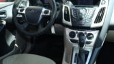 Inside a Ford car: steering wheel with control buttons, center console, and gear shifter visible in the front cabin.
