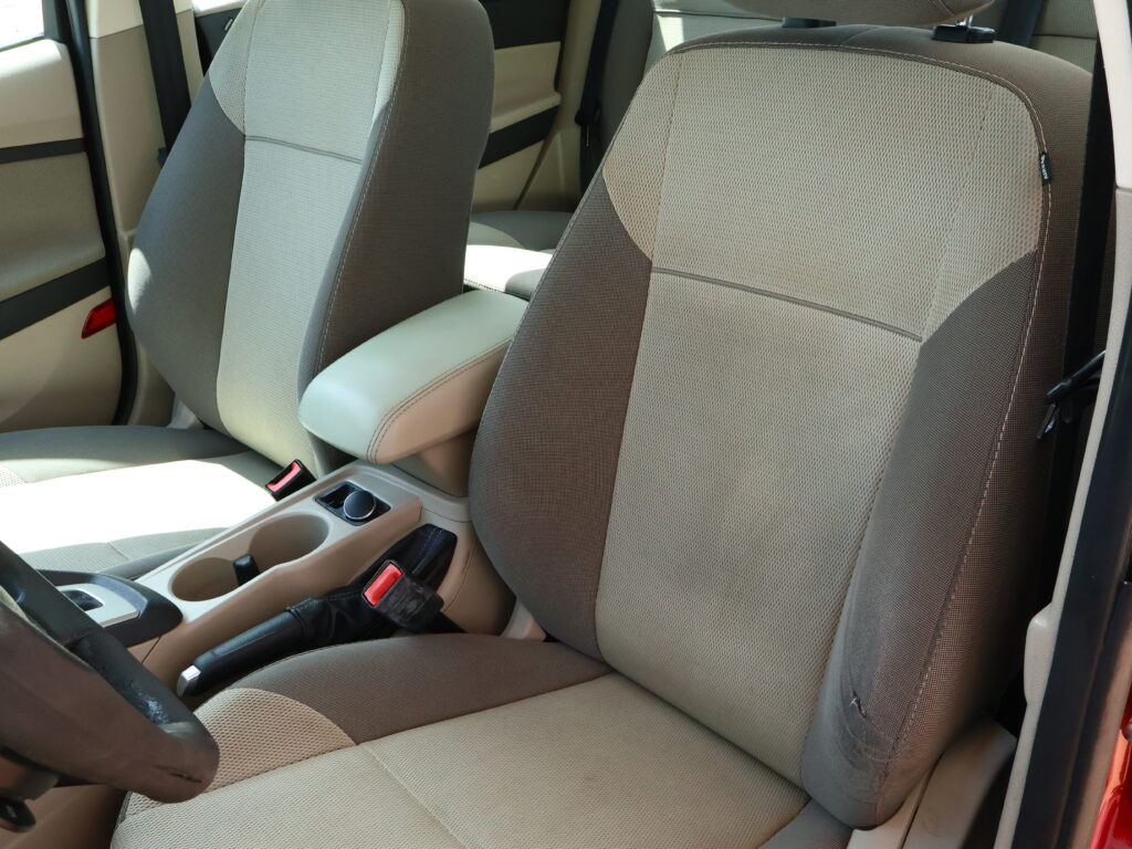 Interior of a car showing beige fabric front seats, center console, and visible seat belts.
