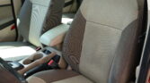Interior of a car showing beige fabric front seats, center console, and visible seat belts.