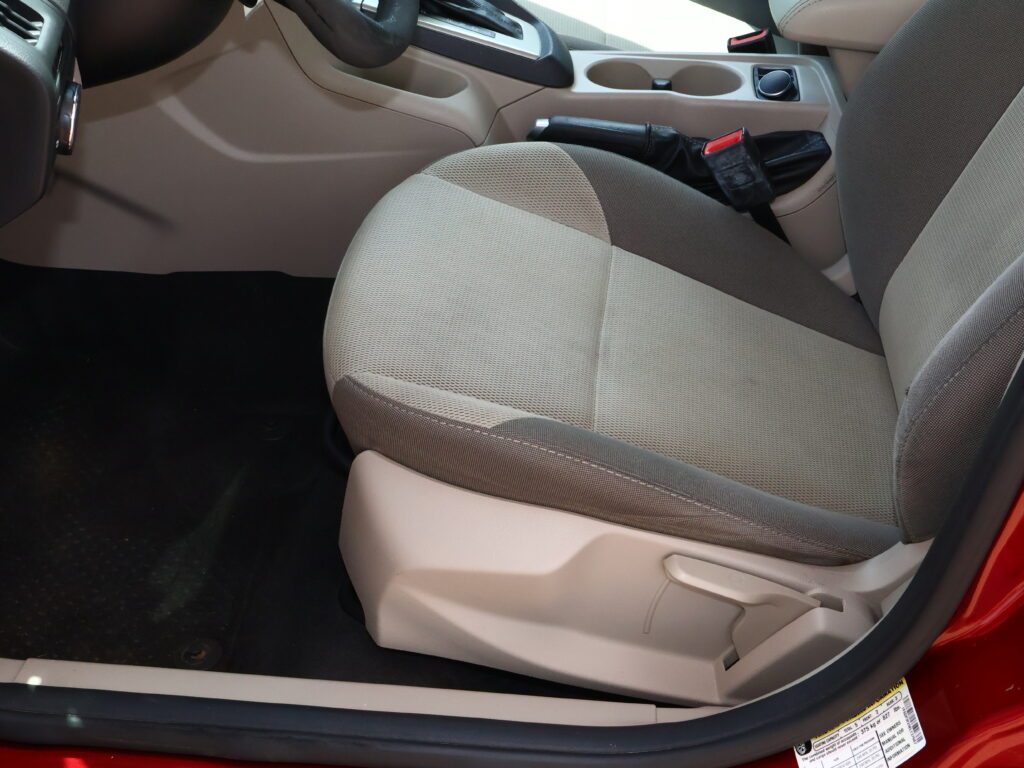 Front passenger seat and center console in a beige car interior, with the seat belt buckle visible near the seat edge