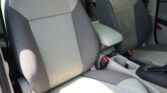 Car interior showing two front seats with light gray fabric and a center armrest between them, plus visible seat belts and cupholders.