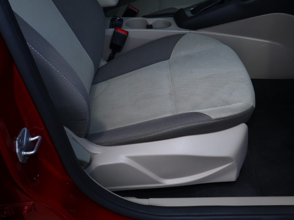 Front passenger seat in light gray fabric with center console and cup holder visible, car door frame at left.