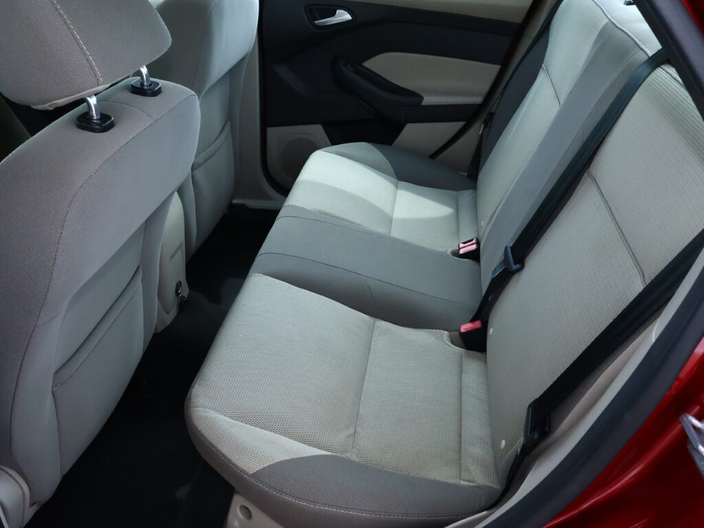 Back seat interior of a car with light gray fabric upholstery, showing two seats and seat belts along the side door panel.