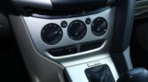 Center console of a car showing climate control dials, hazard button, and a gear selector area; includes A/C and defrost controls and a 'Powered by Microsoft' badge on the panel below.