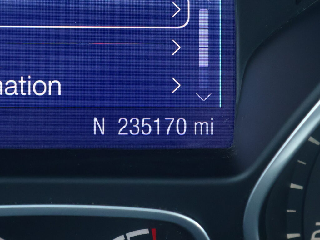 Close-up of a car's digital dashboard/navigation screen showing direction arrows and a distance in miles at the bottom.