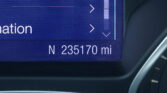 Close-up of a car's digital dashboard/navigation screen showing direction arrows and a distance in miles at the bottom.