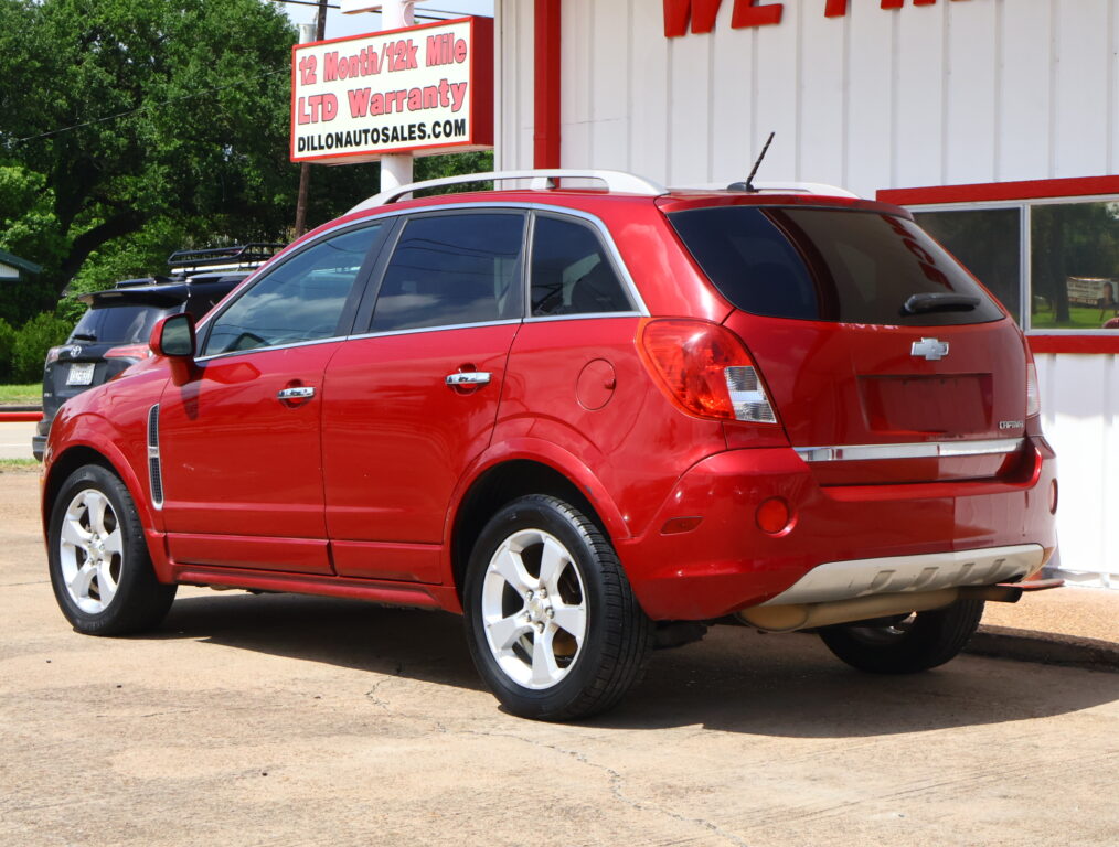 Red Chevrolet Captiva SUV parked outside a dealership, with a bold sign advertising a 12‑month/12k mile warranty.