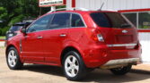 Red Chevrolet Captiva SUV parked outside a dealership, with a bold sign advertising a 12‑month/12k mile warranty.