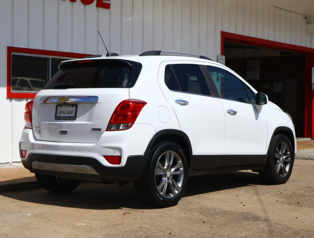 White SUV parked outside a white building with red trim, shown from the rear and passenger side.