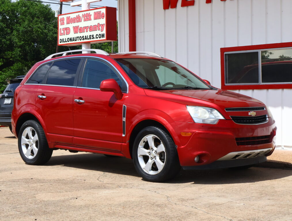 Red Chevy SUV parked in front of a white building with red trim and a sign advertising a 12‑month/12k mile warranty in the background.