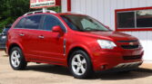 Red Chevy SUV parked in front of a white building with red trim and a sign advertising a 12‑month/12k mile warranty in the background.