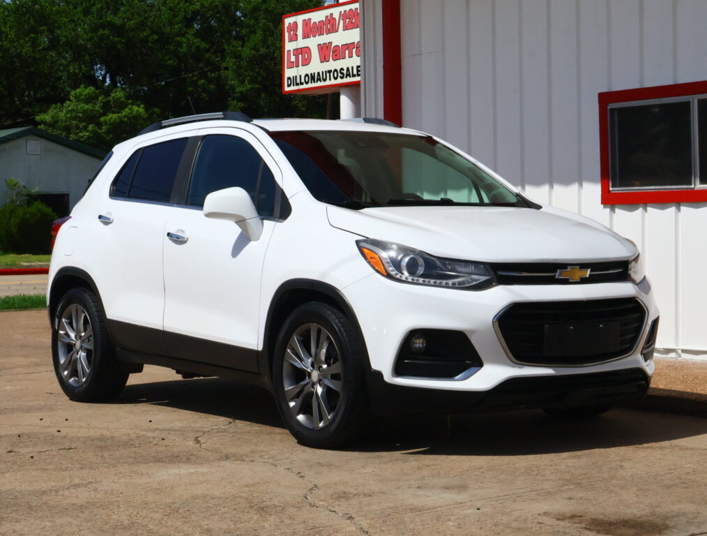 White Chevrolet SUV parked in front of a white building with red trim and a large sign above (auto dealership).