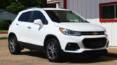 White Chevrolet SUV parked in front of a white building with red trim and a large sign above (auto dealership).