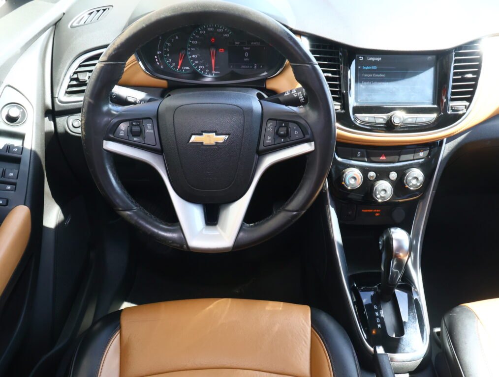 Close-up of a Chevrolet steering wheel with brown leather seats and an digital instrument cluster in a car cabin