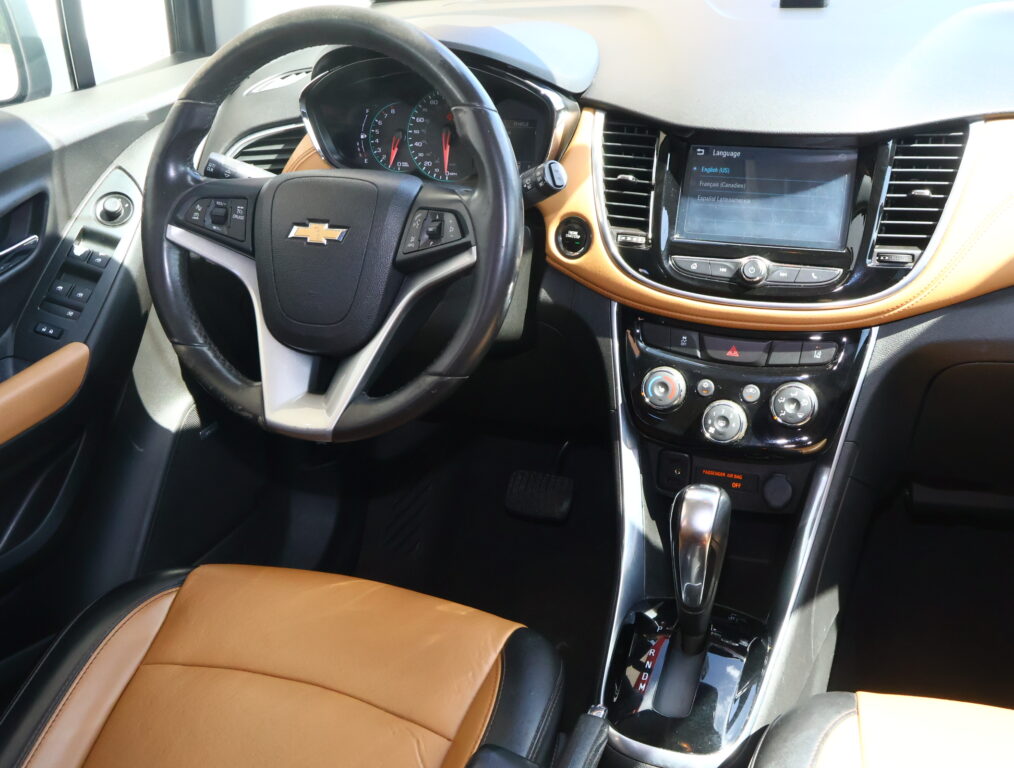 Interior of a Chevrolet car: black steering wheel, tan leather seats, and a center touchscreen display with climate and control buttons visible.