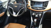 Interior of a Chevrolet car: black steering wheel, tan leather seats, and a center touchscreen display with climate and control buttons visible.