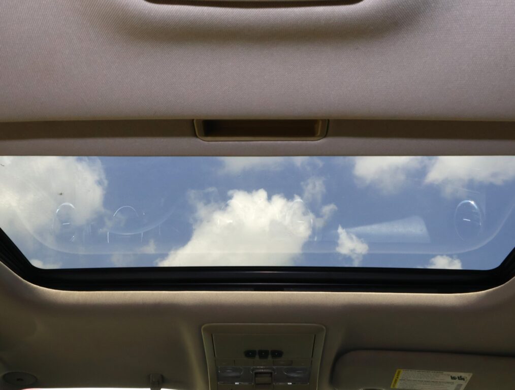 Beige car interior ceiling with an open sunroof revealing a blue sky and scattered white clouds.