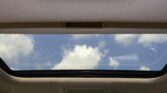 Beige car interior ceiling with an open sunroof revealing a blue sky and scattered white clouds.